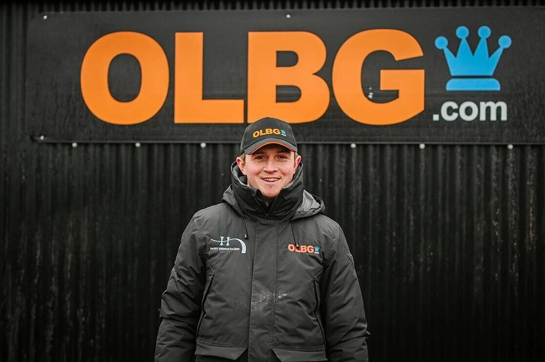 Harry Derham standing by an OLBG sign at Upper Farm Stables